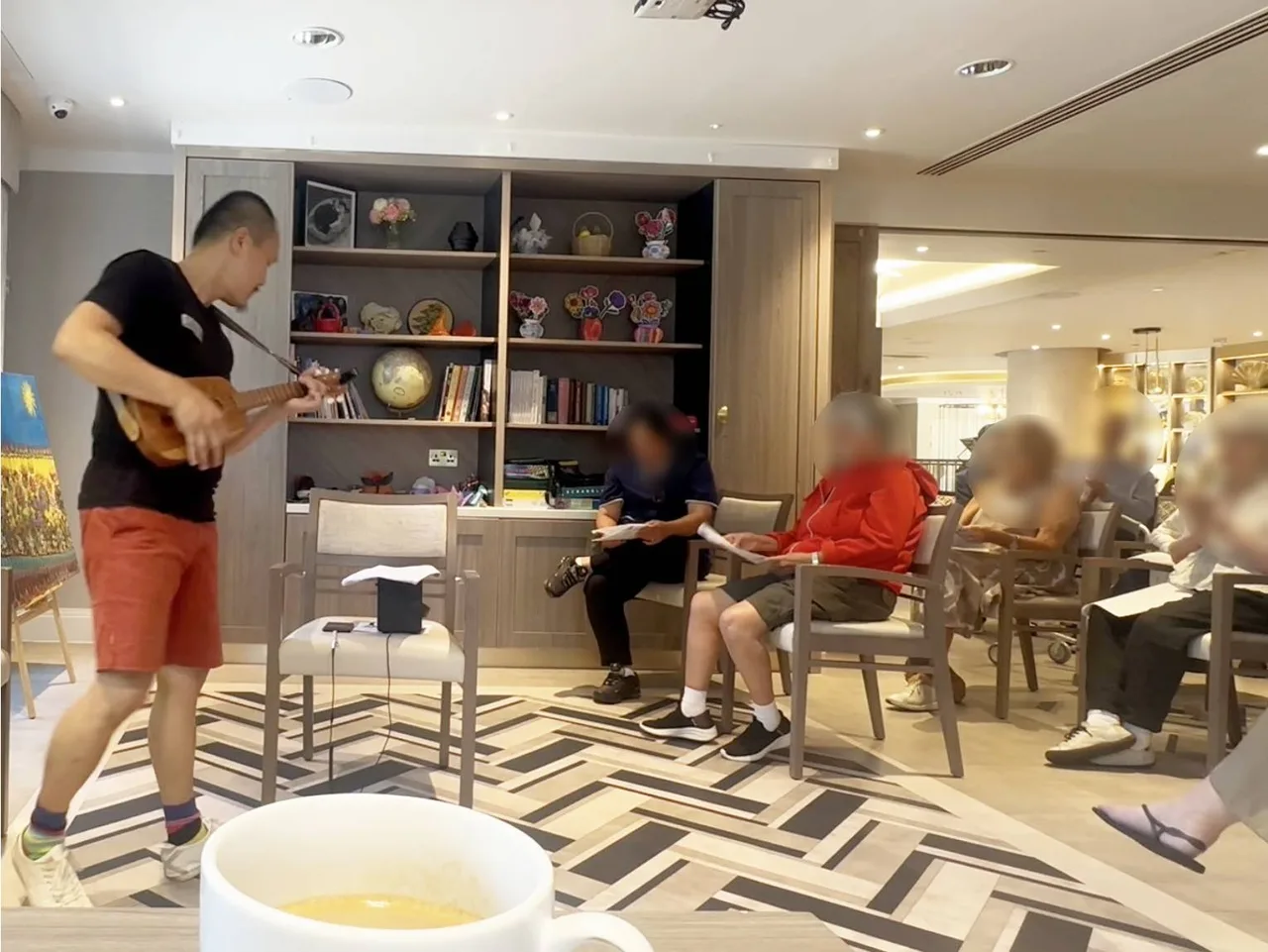 Frven Lim playing ukulele for elderly residents in a modern care home in Hertfordshire — active musical engagement for resident wellbeing