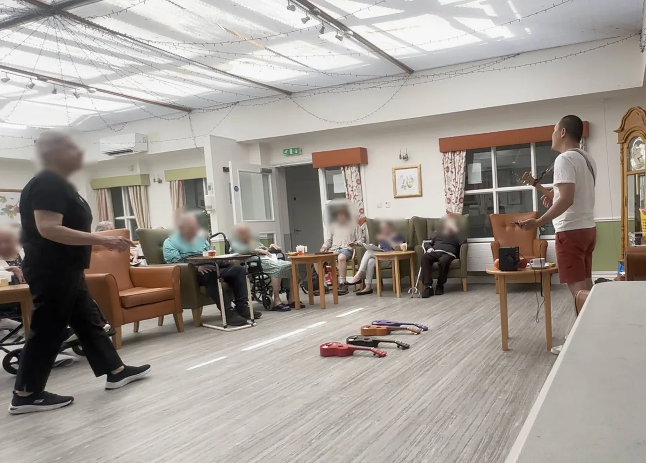 Frven Lim performing live ukulele for care home residents in a bright activity room — boosting resident mood and social connection through music