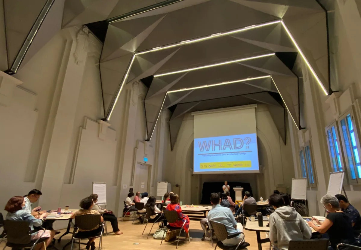 Frven Lim presenting to an audience seated around tables in a workshop setting