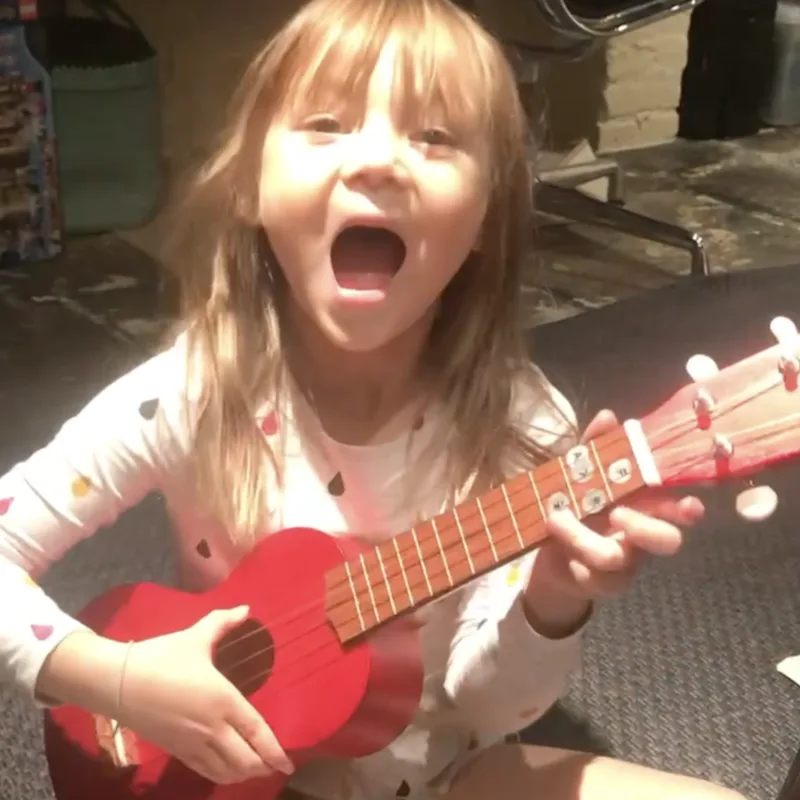 Young girl joyfully singing and playing ukulele